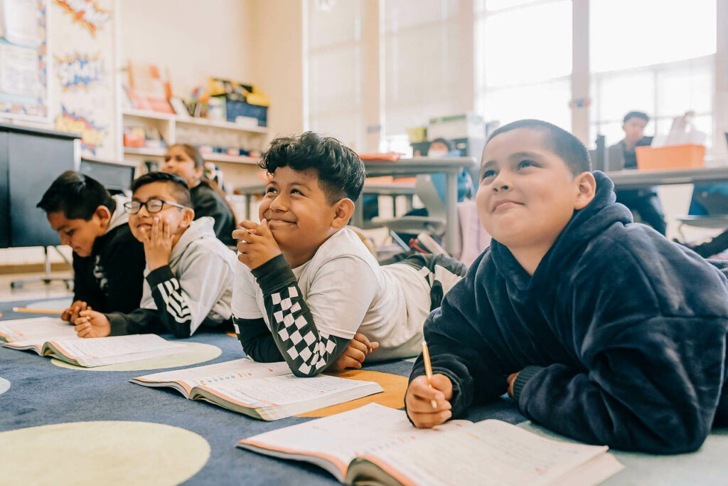 Students sitting on floor of classroom with books looking up